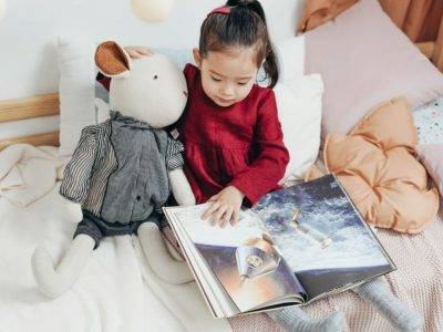 fillette lisant un album jeunesse sur un lit avec une peluche